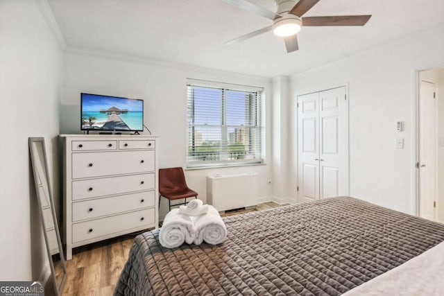 bedroom featuring a closet, radiator heating unit, crown molding, hardwood / wood-style flooring, and ceiling fan