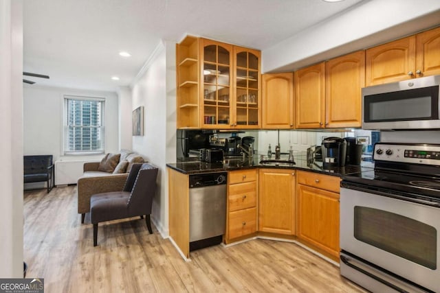 kitchen featuring stainless steel appliances, dark stone counters, tasteful backsplash, ornamental molding, and light wood-type flooring