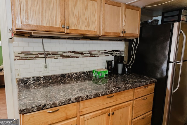 kitchen with hardwood / wood-style floors, decorative backsplash, stainless steel fridge, and dark stone counters