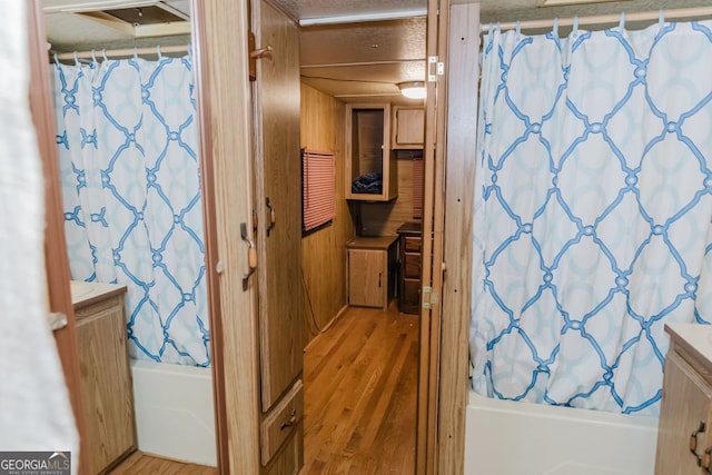 bathroom with wooden walls, shower / bath combination with curtain, vanity, and wood-type flooring