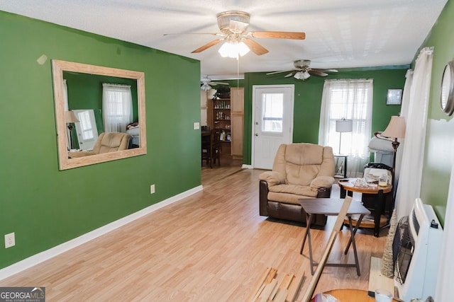 living area with heating unit, ceiling fan, and light hardwood / wood-style flooring