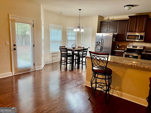 kitchen featuring a breakfast bar, light stone counters, appliances with stainless steel finishes, decorative light fixtures, and dark wood-type flooring