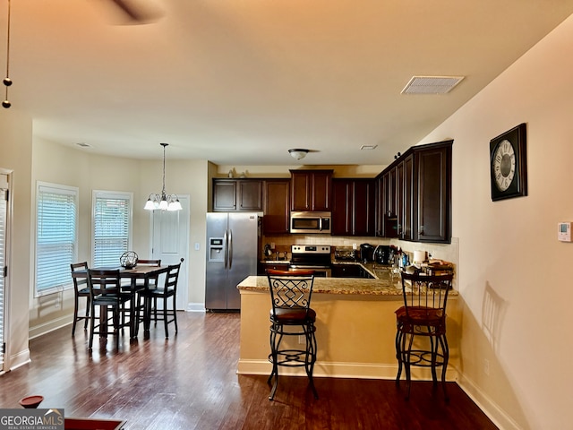 kitchen featuring dark hardwood / wood-style flooring, light stone counters, a kitchen breakfast bar, appliances with stainless steel finishes, and decorative light fixtures