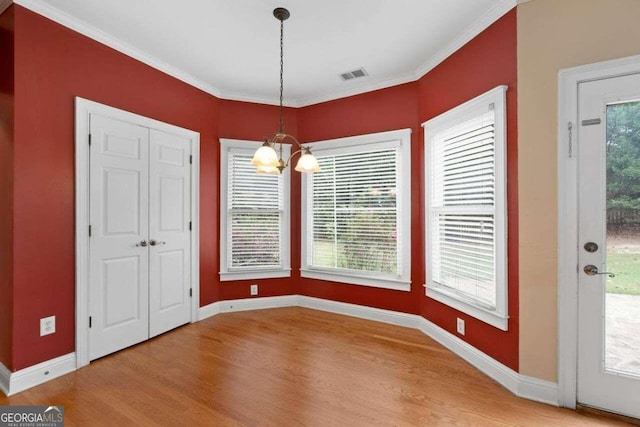 unfurnished dining area with ornamental molding, hardwood / wood-style floors, a wealth of natural light, and a notable chandelier