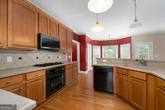 kitchen with decorative backsplash, hanging light fixtures, black appliances, sink, and light wood-type flooring