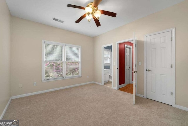 unfurnished bedroom featuring light colored carpet, ceiling fan, and ensuite bath