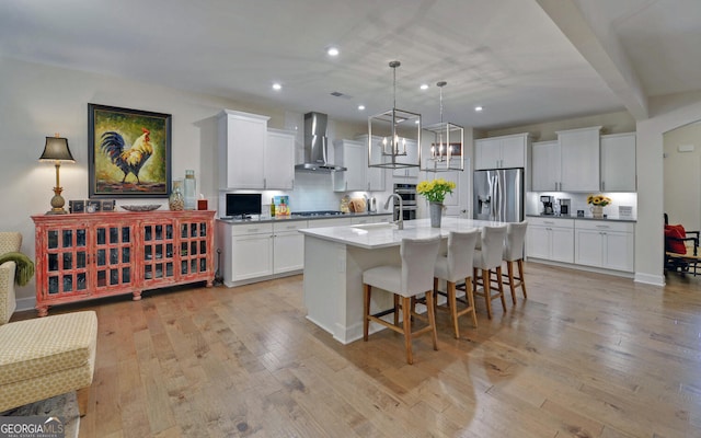 kitchen with white cabinets, stainless steel refrigerator with ice dispenser, wall chimney exhaust hood, a kitchen island with sink, and light hardwood / wood-style flooring