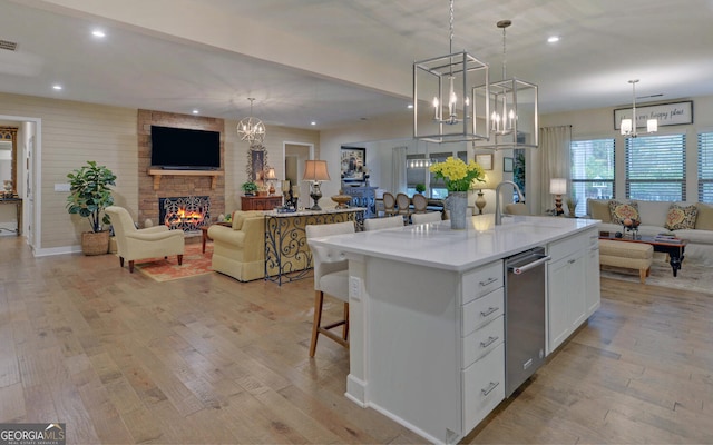 kitchen featuring light hardwood / wood-style floors, pendant lighting, an island with sink, white cabinetry, and a fireplace