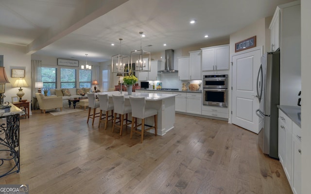 kitchen with stainless steel appliances, wall chimney range hood, white cabinetry, and an island with sink