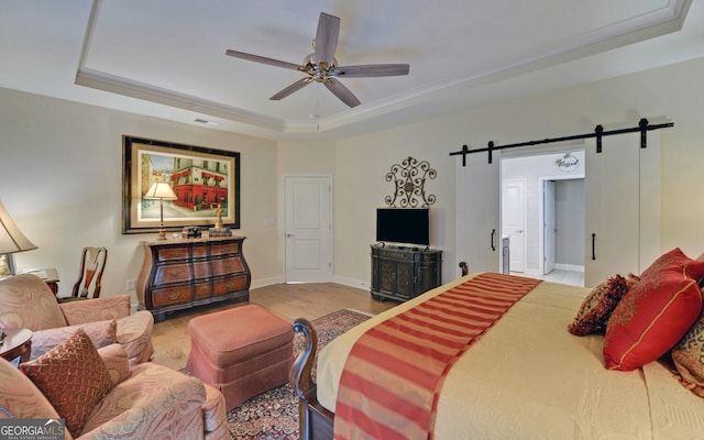 bedroom featuring light wood-type flooring, a barn door, ceiling fan, and a raised ceiling