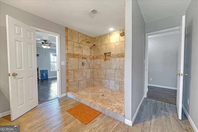 bathroom with tiled shower, ceiling fan, wood-type flooring, and a textured ceiling