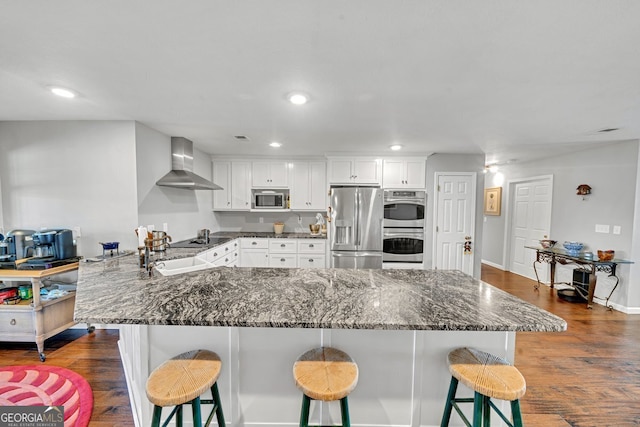 kitchen with white cabinets, a breakfast bar, wall chimney exhaust hood, and appliances with stainless steel finishes