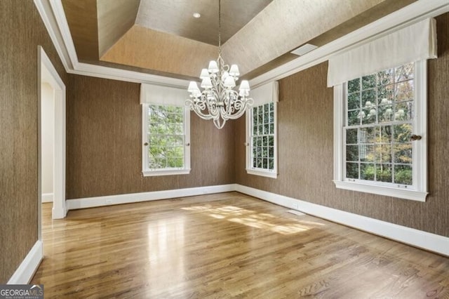 unfurnished dining area featuring a raised ceiling, plenty of natural light, an inviting chandelier, and hardwood / wood-style flooring