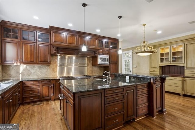 kitchen featuring sink, decorative light fixtures, a center island with sink, hardwood / wood-style flooring, and stainless steel microwave