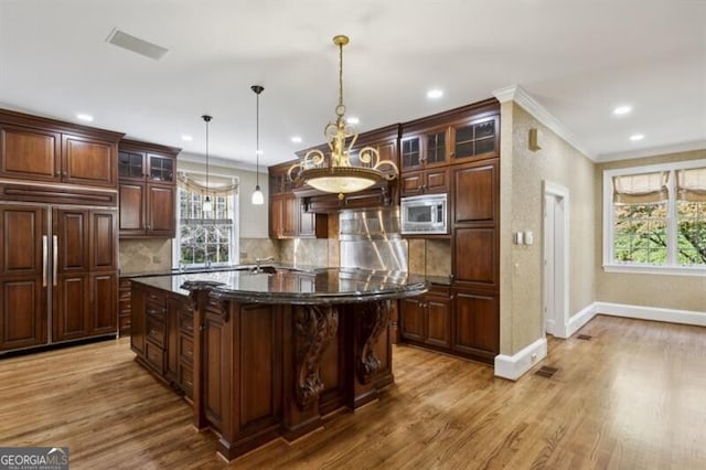 kitchen with light wood-type flooring, a wealth of natural light, pendant lighting, built in appliances, and a kitchen island