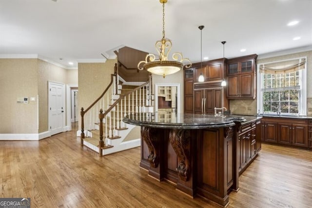 kitchen featuring hardwood / wood-style flooring, decorative light fixtures, paneled refrigerator, and a center island with sink