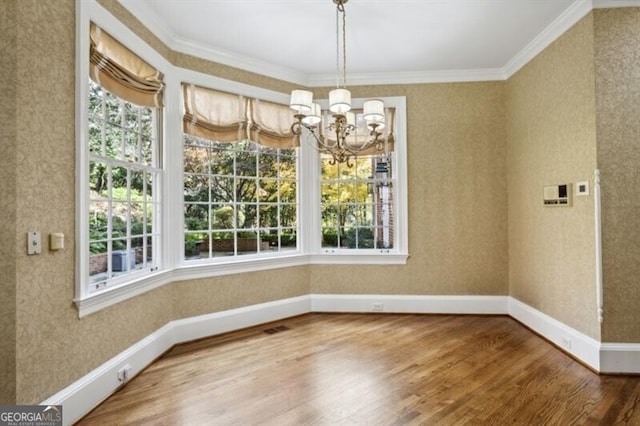 unfurnished dining area with an inviting chandelier, ornamental molding, and hardwood / wood-style flooring