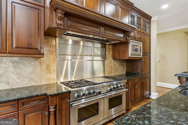 kitchen featuring decorative backsplash, dark stone countertops, ornamental molding, light wood-type flooring, and appliances with stainless steel finishes