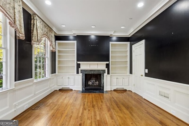 unfurnished living room featuring a high end fireplace, light hardwood / wood-style floors, and crown molding