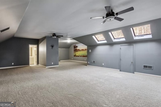 additional living space with vaulted ceiling with skylight, ceiling fan, and light carpet