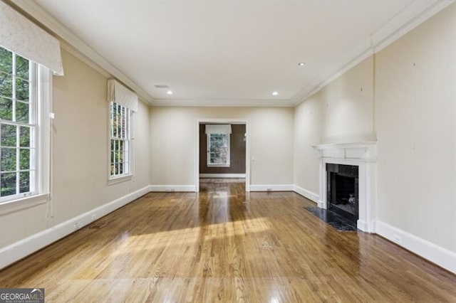 unfurnished living room featuring a large fireplace, hardwood / wood-style flooring, plenty of natural light, and crown molding