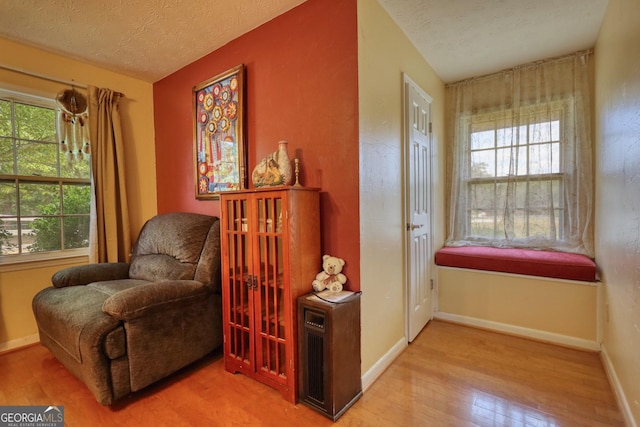 living area with a wealth of natural light, a textured ceiling, baseboards, and wood finished floors