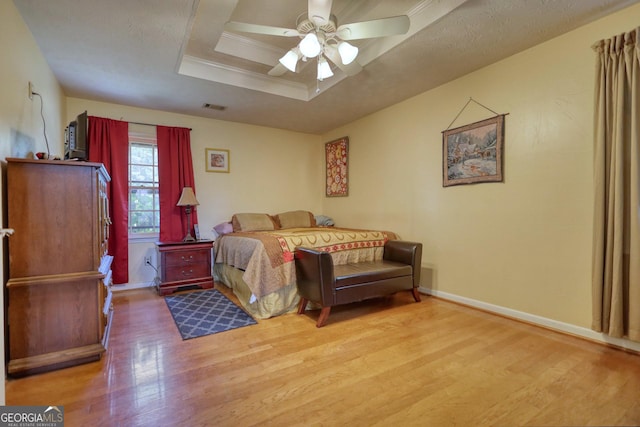 bedroom featuring a raised ceiling, ceiling fan, ornamental molding, and light wood-type flooring