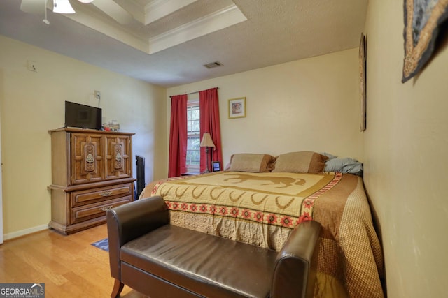 bedroom with ceiling fan, crown molding, light hardwood / wood-style flooring, and a tray ceiling