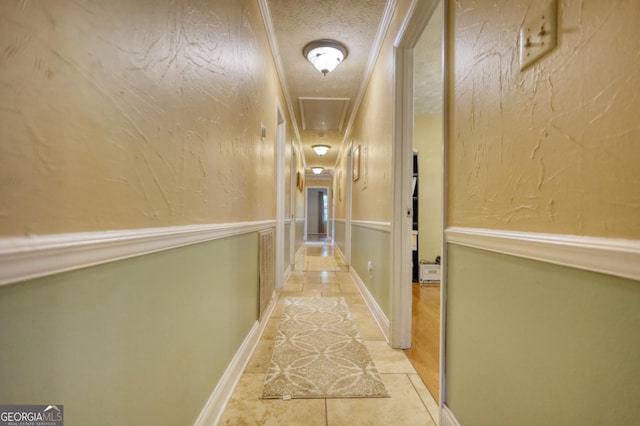 hall with a textured ceiling, a textured wall, light tile patterned flooring, baseboards, and attic access