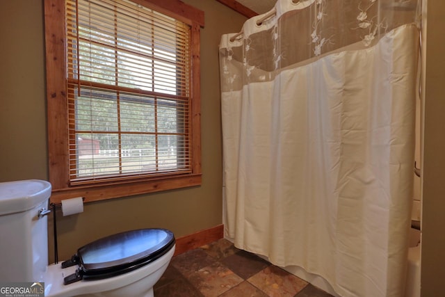 full bathroom featuring toilet, stone finish floor, and baseboards