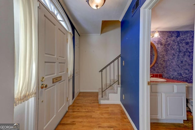 entryway with ornamental molding and light hardwood / wood-style floors