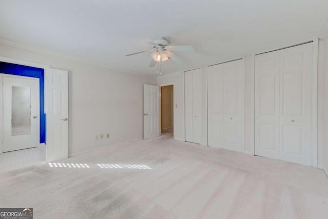 unfurnished bedroom featuring multiple closets, ornamental molding, light colored carpet, and ceiling fan