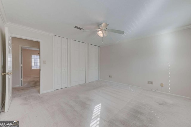 unfurnished bedroom featuring ceiling fan, light colored carpet, crown molding, and two closets