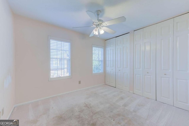 unfurnished bedroom with light carpet, two closets, and ceiling fan