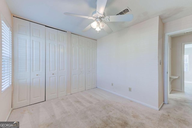 unfurnished bedroom with two closets, light colored carpet, and ceiling fan