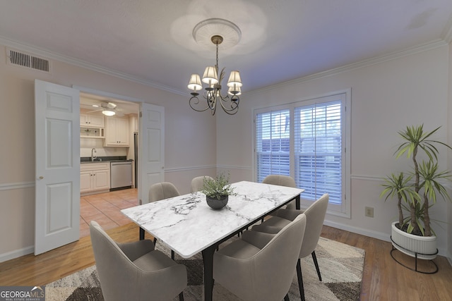 dining room with crown molding, an inviting chandelier, sink, and light hardwood / wood-style floors