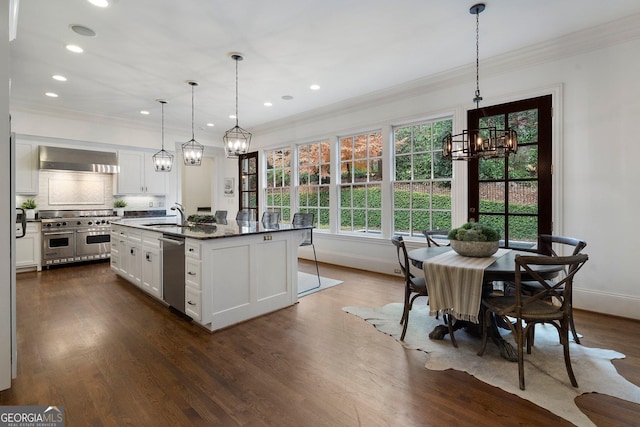 kitchen with a center island with sink, white cabinets, wall chimney exhaust hood, dark stone countertops, and stainless steel appliances