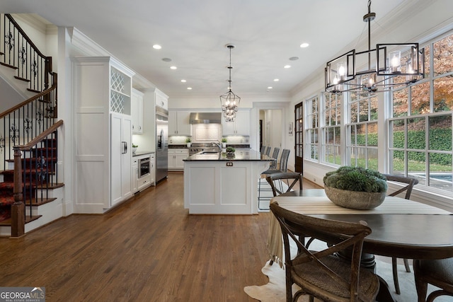 kitchen featuring wall chimney exhaust hood, dark wood-type flooring, stainless steel appliances, decorative light fixtures, and white cabinets