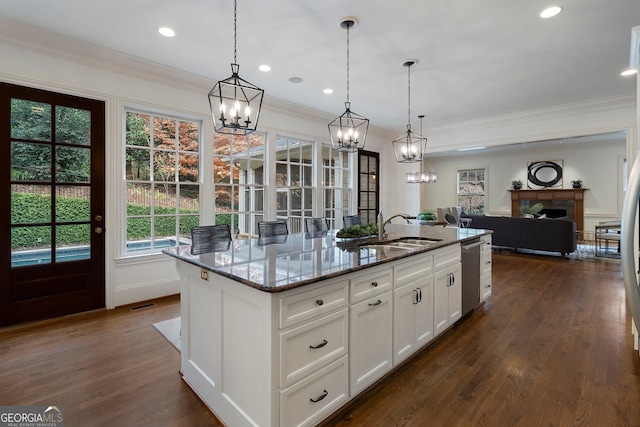 kitchen featuring dark stone countertops, white cabinetry, a center island with sink, and pendant lighting