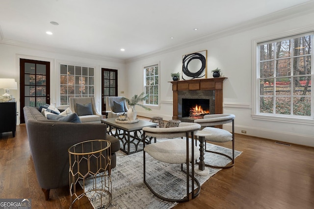 living room featuring a healthy amount of sunlight, a fireplace, wood-type flooring, and ornamental molding