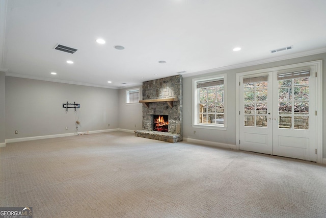 unfurnished living room featuring crown molding, a stone fireplace, light carpet, and a wealth of natural light