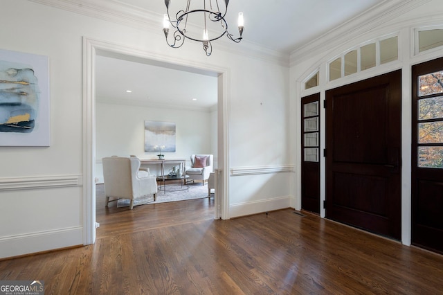 foyer entrance with dark wood-type flooring, an inviting chandelier, and ornamental molding