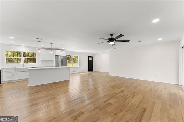 unfurnished living room with ceiling fan, sink, light hardwood / wood-style flooring, and ornamental molding