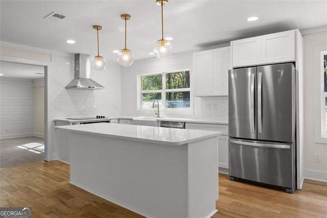 kitchen featuring stainless steel appliances, wall chimney range hood, white cabinets, and hanging light fixtures