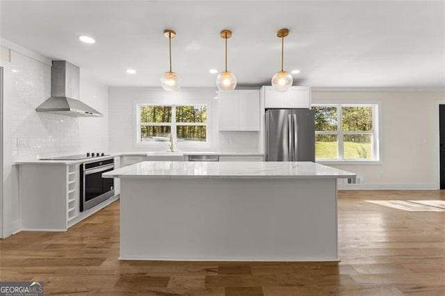 kitchen featuring plenty of natural light, wall chimney range hood, appliances with stainless steel finishes, and white cabinets