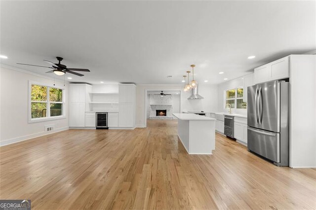 kitchen with light hardwood / wood-style floors, white cabinets, pendant lighting, a fireplace, and stainless steel fridge