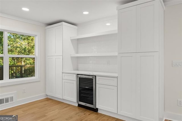 bar featuring backsplash, white cabinetry, wine cooler, and light wood-type flooring