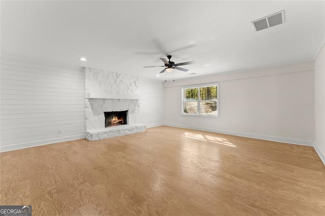 unfurnished living room with ceiling fan, a stone fireplace, light hardwood / wood-style flooring, and crown molding