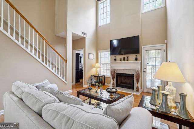 living room with a wealth of natural light, a towering ceiling, light hardwood / wood-style flooring, and a premium fireplace