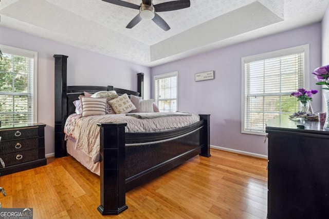 bedroom with light wood-type flooring, multiple windows, ceiling fan, and a tray ceiling